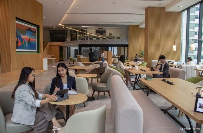 Two women sit at a round table in a modern coworking cafe, discussing a tablet nearby.