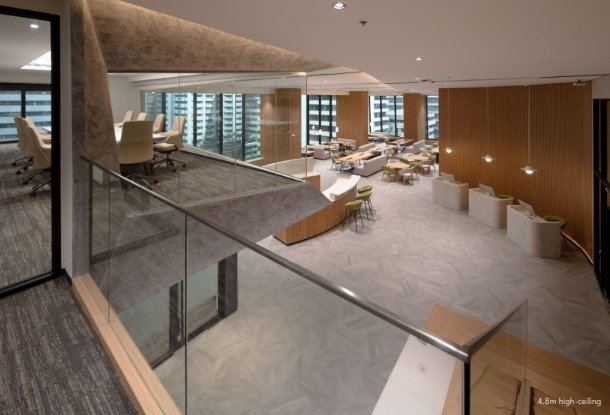 Open-plan corporate lounge with glass railing, curved wooden reception, and a variety of seating on two levels.