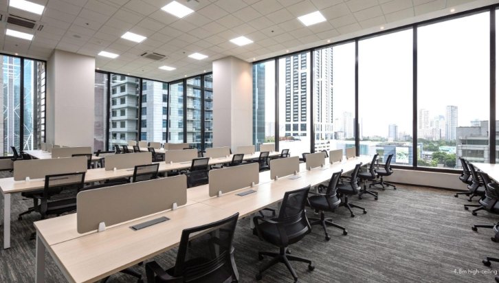 Open-plan conference room with long rows of desks, ergonomic chairs, and partition screens, overlooking a city skyline.