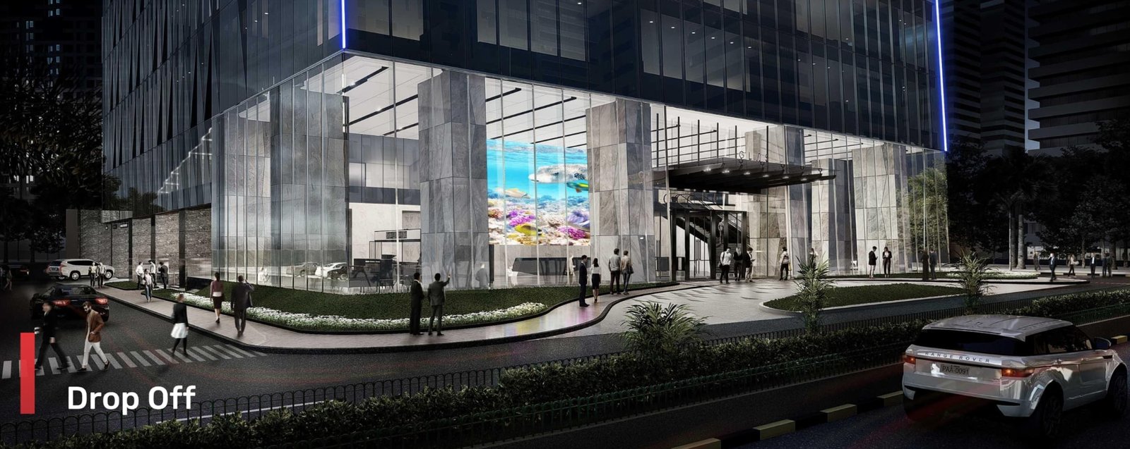 Screenshot_18-6-2026_17210_glas.ph Nighttime view of a glass modern building with a covered drop-off area, pedestrians on the sidewalk, and cars along the curb; a bright aquarium-style screen is visible inside. The word 'Drop Off' appears at left.