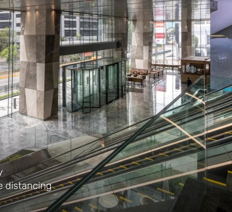 Modern hotel lobby interior with tall glass walls, marble floor, and escalators; on-screen text reads 'Grand Lobby' with notes about an 8.5-meter high space, safe distancing, and crystal revolving doors.