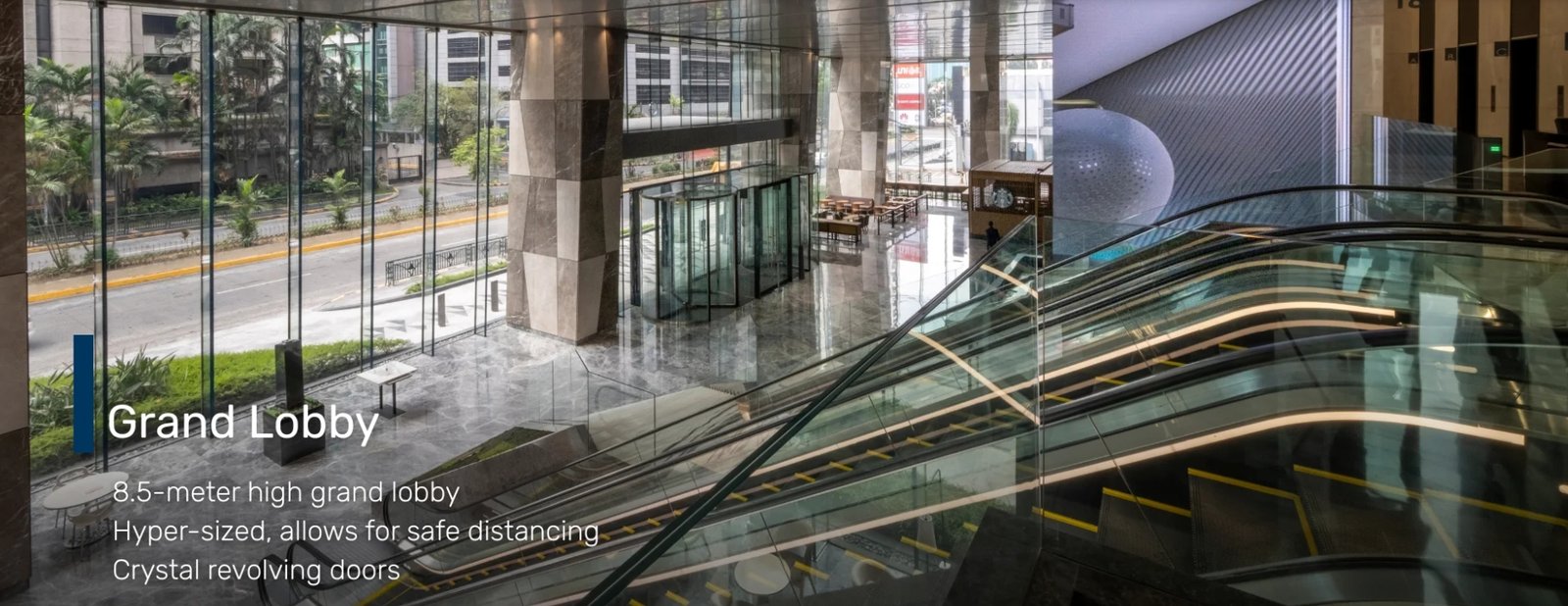 Screenshot_18-6-2026_172226_glas.ph Modern hotel lobby interior with tall glass walls, marble floor, and escalators; on-screen text reads 'Grand Lobby' with notes about an 8.5-meter high space, safe distancing, and crystal revolving doors.