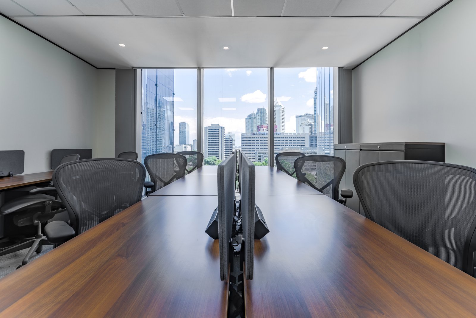 Empty conference room with a long wooden table and mesh chairs, large city view through floor‑to‑ceiling windows.