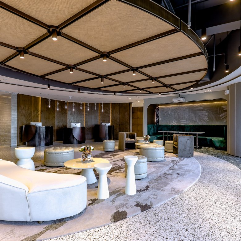 Modern hotel lobby lounge with a domed, grid-pattern ceiling and pendant lights overseeing white curved sofas and round ottomans.
