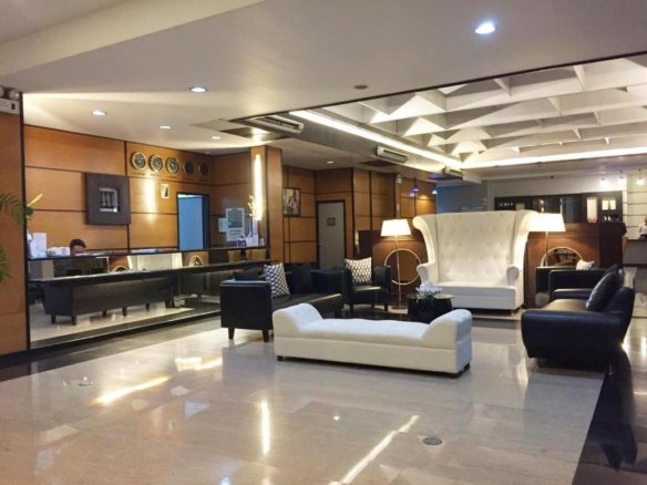 Hotel lobby lounge with a large white tufted chair, black sofas, and a white ottoman around a central coffee table in a modern reception area.