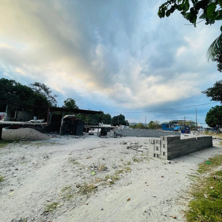 Construction site with stacked concrete blocks and scaffolding under a cloudy sky, trees in the background