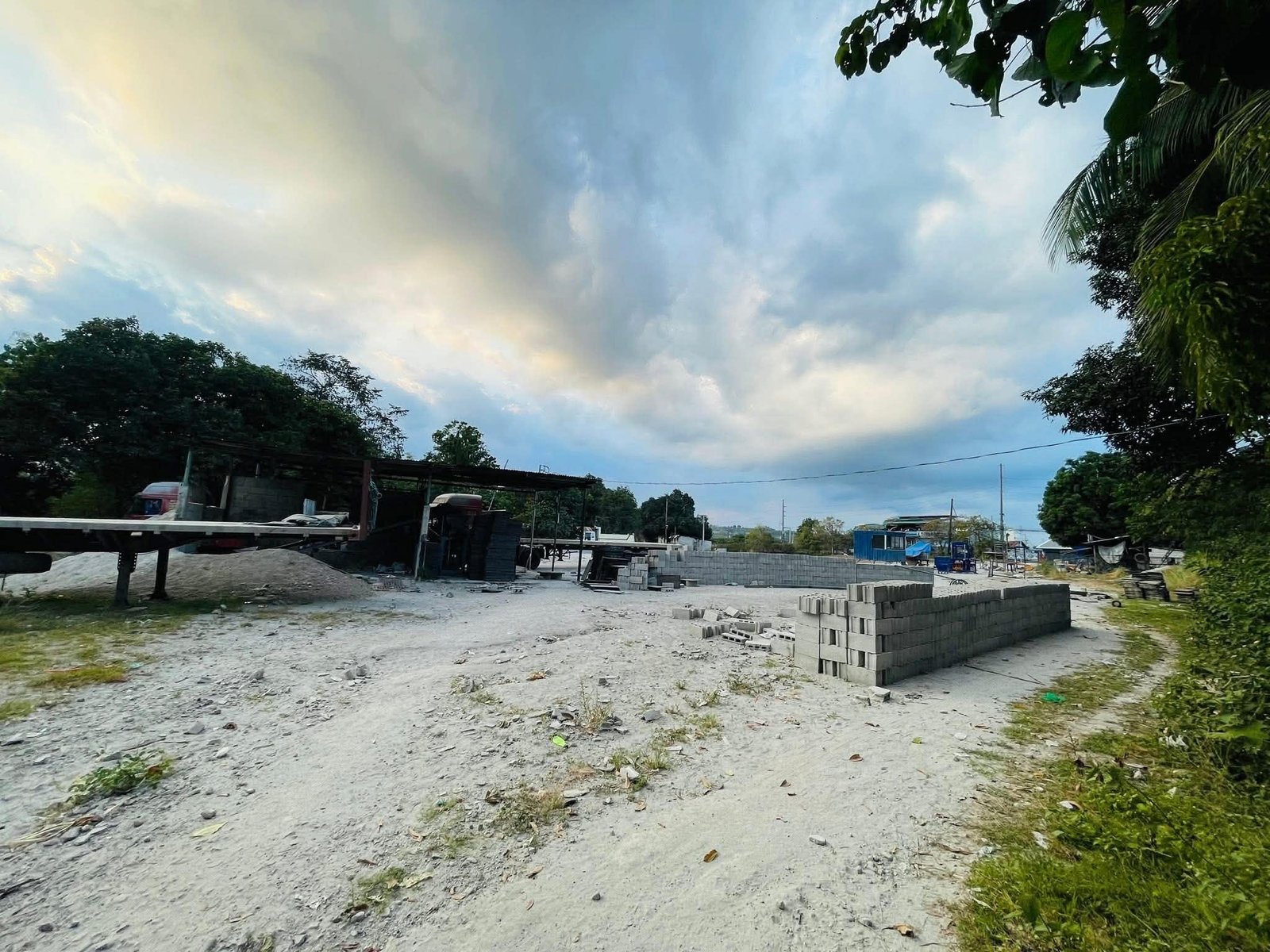 Construction site with stacked concrete blocks and scaffolding under a cloudy sky, trees in the background