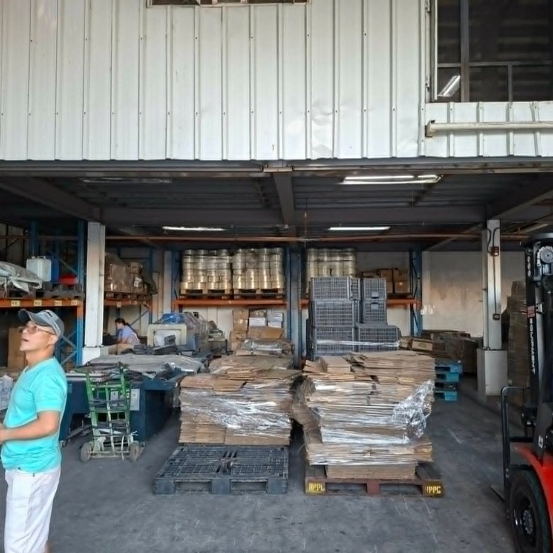 Warehouse with stacked pallets and shelves; a worker in a turquoise shirt stands near the entrance.