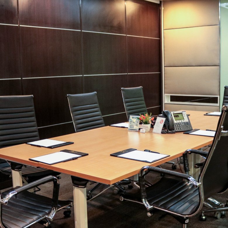 Conference room with a long wooden table, black leather chairs, and a desk phone at the center