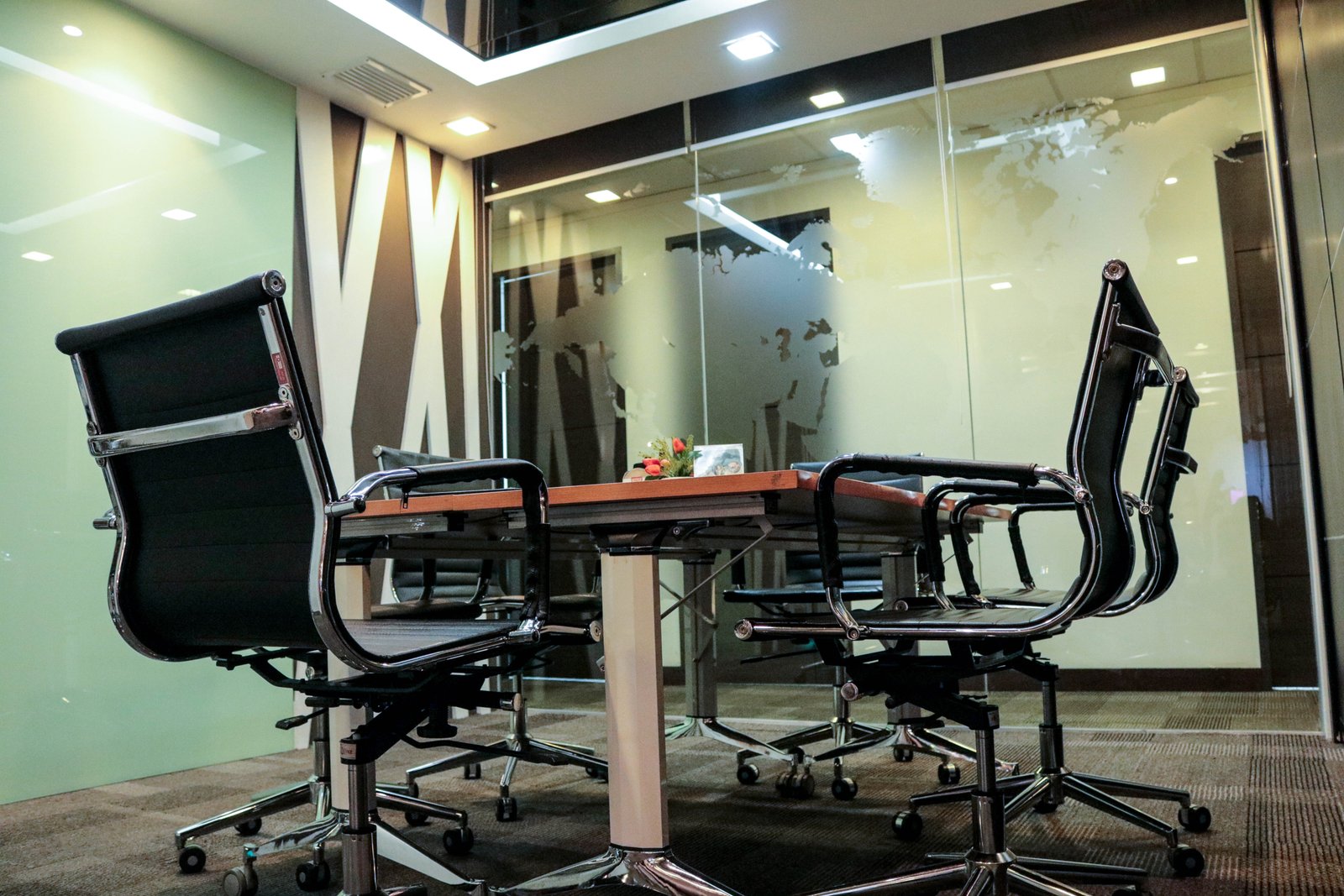 Conference room with glass walls and a long table surrounded by black office chairs on wheels, in a modern office setting