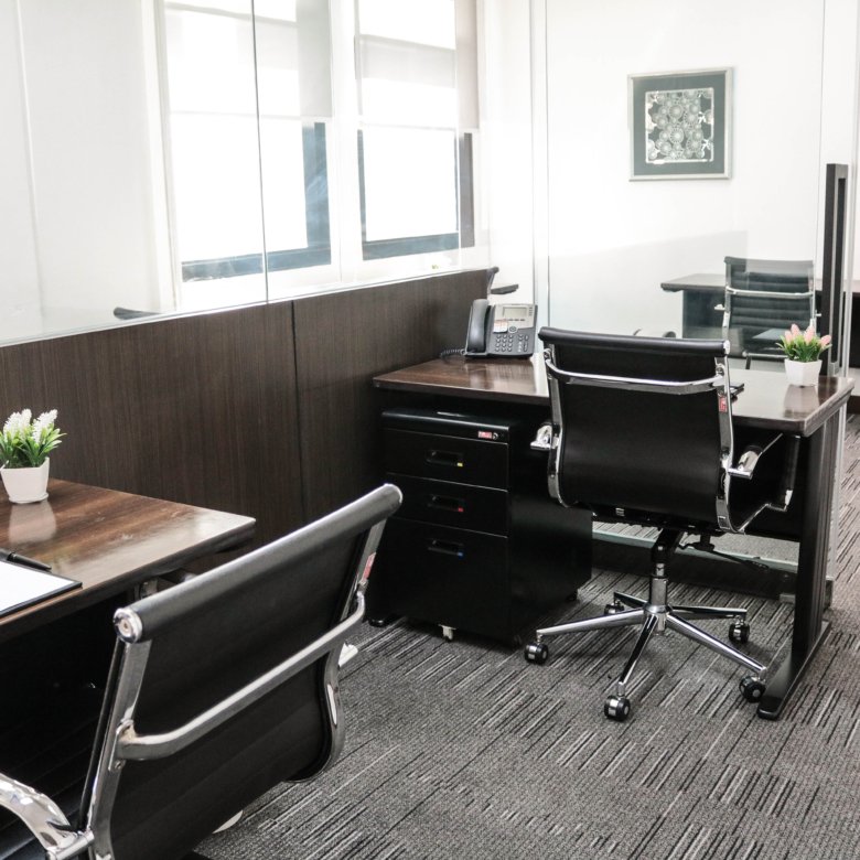 Open office workspace with dark wood desks, black leather chairs, a landline phone, and small potted plants along a glass divider.