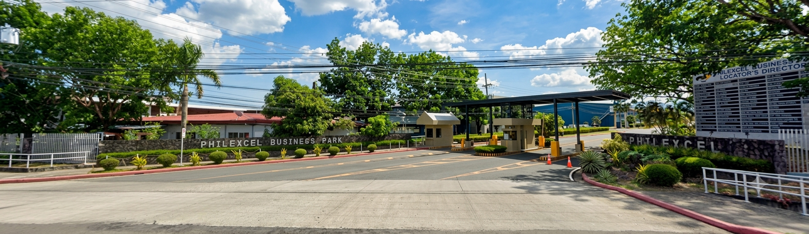 Entrance to Philexcel Business Park with a gated security booth and landscaped shrubs under a blue sky.