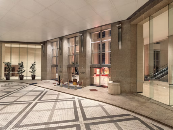 Spacious lobby with stone pillars, glass walls, potted plants, and an escalator visible on the right.