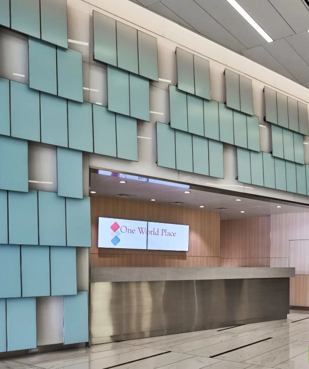 Reception desk in a modern lobby with teal wall panels and a metal counter, displaying a sign that reads 'One World Place'.