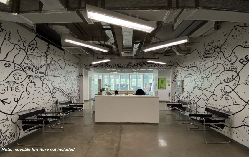 Reception desk in a bright open lobby with mural-covered walls and black benches along both sides, ceiling lights above