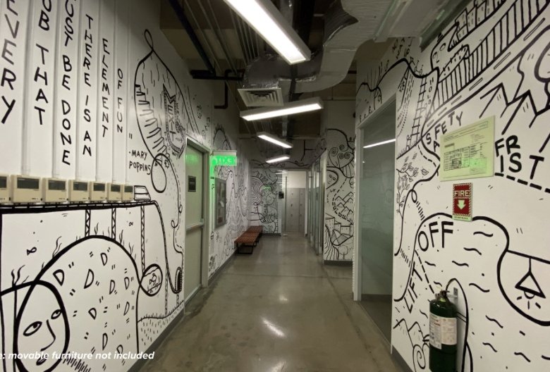 Long corridor with white walls covered in black doodle artwork, overhead lights, and a bench under a green exit sign.