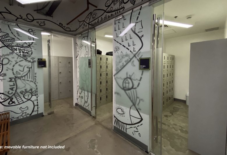 Industrial hallway with glass doors covered in doodle graffiti and a row of metal lockers behind. Concrete floor, bright lighting.