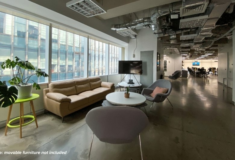 Modern office lounge with a beige sofa, round coffee tables, and gray chairs by large windows.