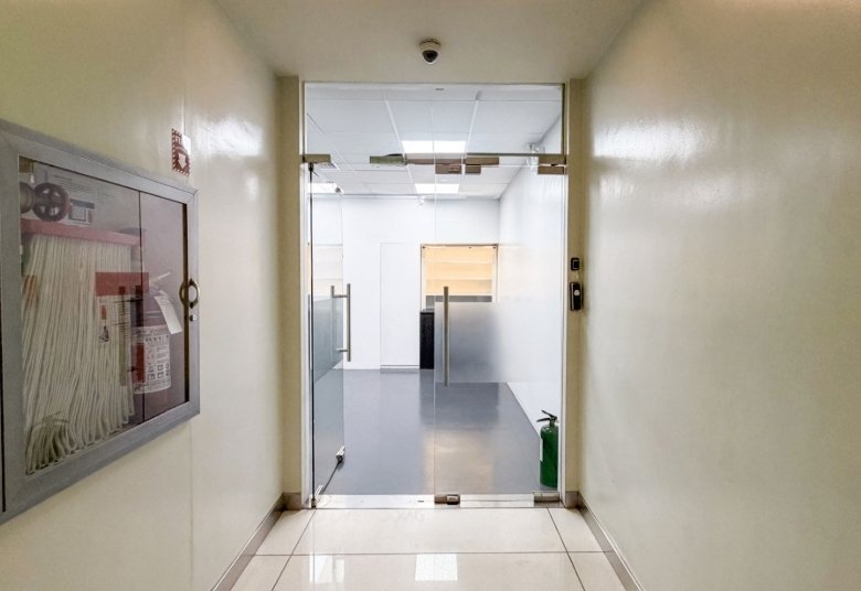 Glass double doors open into a bright, minimalist hallway with a green fire extinguisher on the right side near the door.
