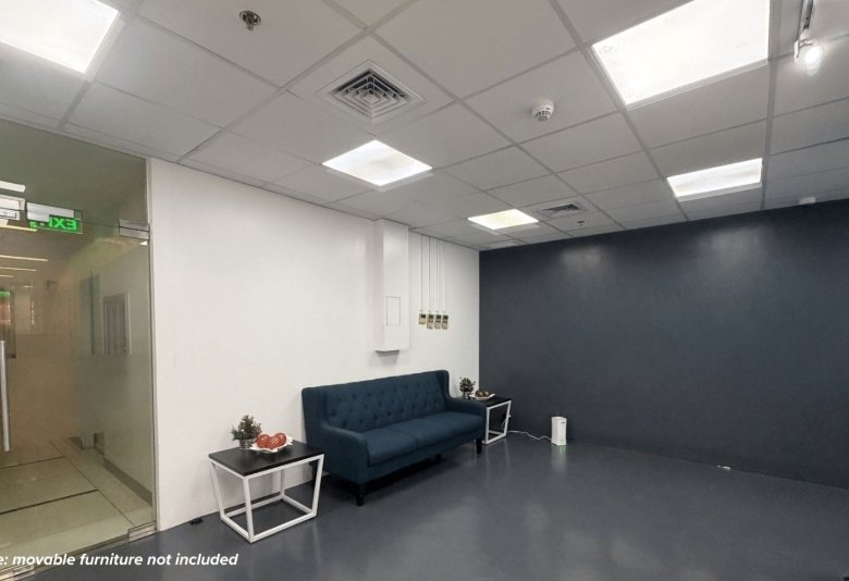 Office reception/waiting area: dark blue tufted sofa with two small glass tables and potted plants, white walls, dark blue accent wall, glass doorway on the left.