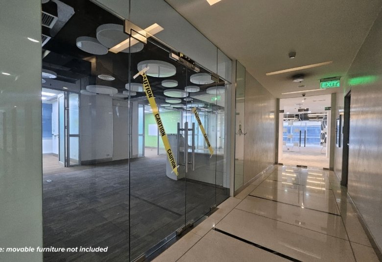 Glass-walled conference room in an office hallway taped off with yellow CAUTION tape; note reads 'Note: movable furniture not included' in the lower-left corner.