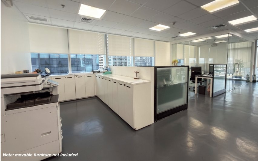 Modern open-plan office with white cabinets and a copier along a curved counter, glass-walled workstations, and a cityscape outside the windows.