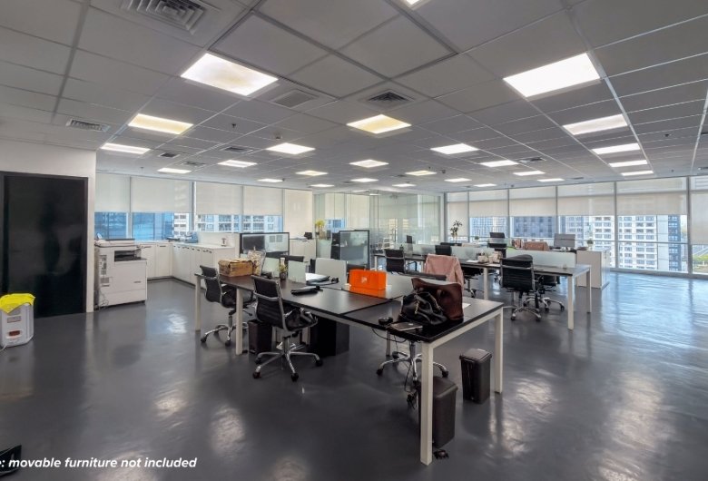 Open-plan office with several desks, computers, and swivel chairs, overlooking city skyline through large windows; note says movable furniture not included.
