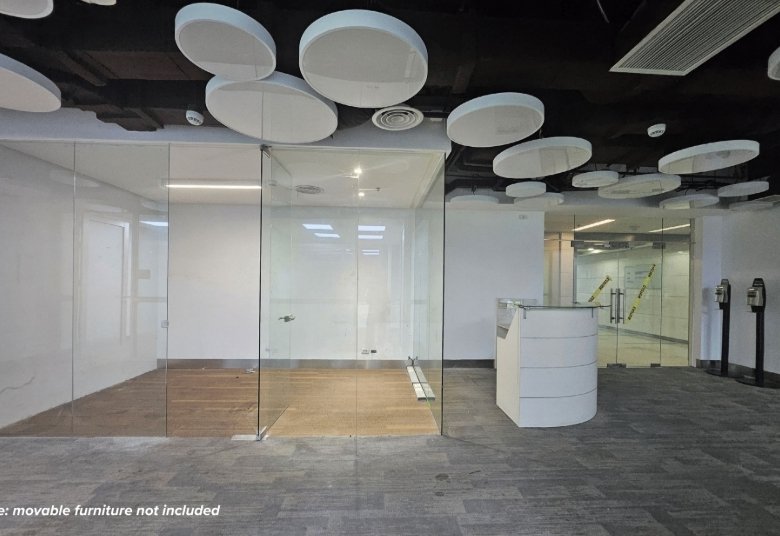 Glass-walled meeting room in a modern office lobby, with a white reception desk and circular ceiling acoustic panels.