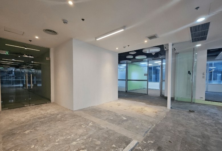 Empty office space under renovation with glass doors, white walls, and exposed concrete flooring.