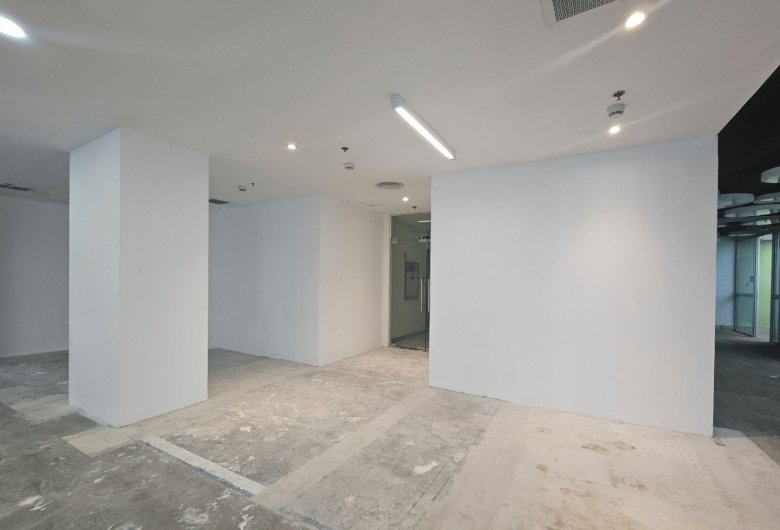Empty, modern office space under renovation with white walls, two large columns, and an unfinished concrete floor; glass door in back.