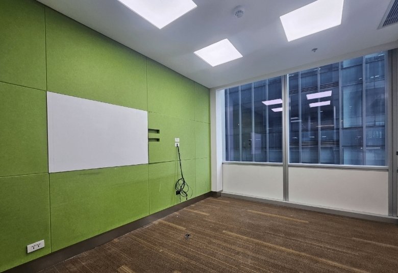 Empty conference/meeting room with green acoustic wall panels, a whiteboard, and tangled cables by the outlet.