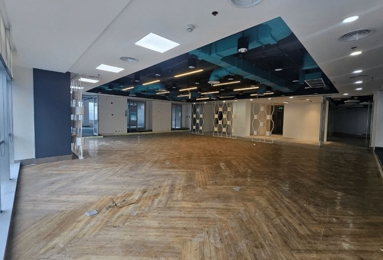 Open, empty office space under renovation with teal exposed ductwork and hexagonal partition walls.