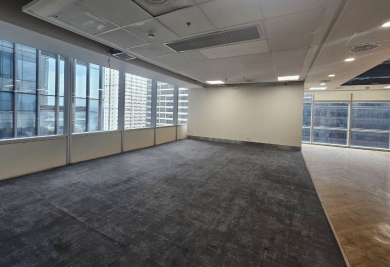 Empty open-plan office space with large windows and cityscape views, neutral carpet, and white walls.