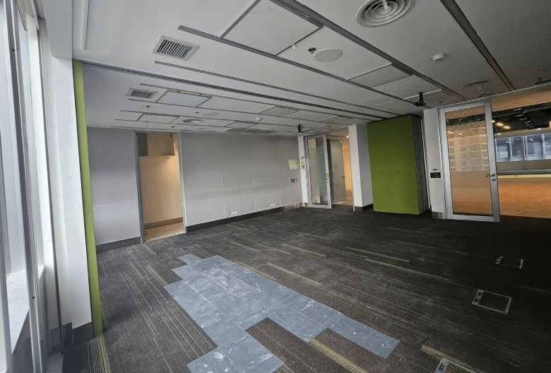 Empty office space with gray walls, green pillar, glass doors, and a patchy blue-gray carpet in daylight
