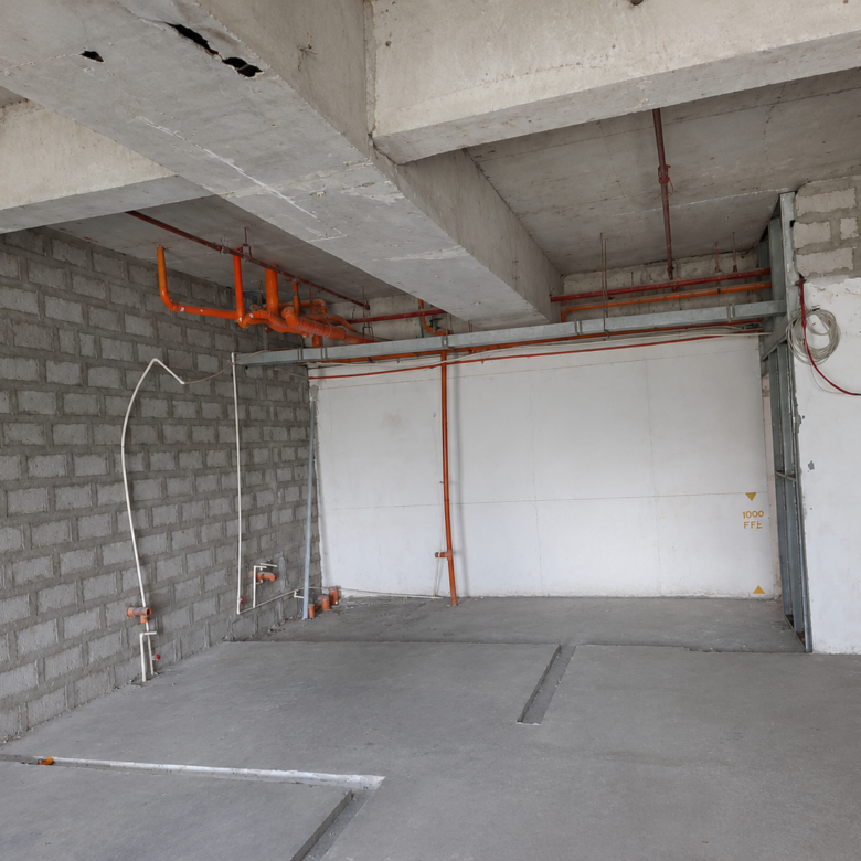 Under-construction room with orange plumbing pipes along the ceiling, concrete beams, and exposed wiring on the walls.