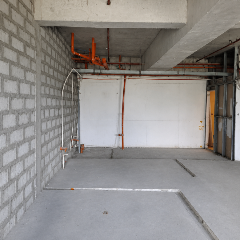 Construction site interior with exposed orange pipes along the ceiling and unfinished concrete walls and floor.