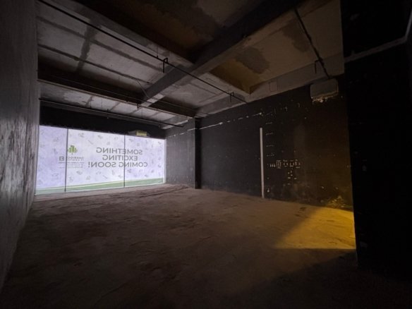 Dimly lit interior of a construction site with exposed concrete beams, pipes, and a dark wall; appears unfinished and industrial at night.