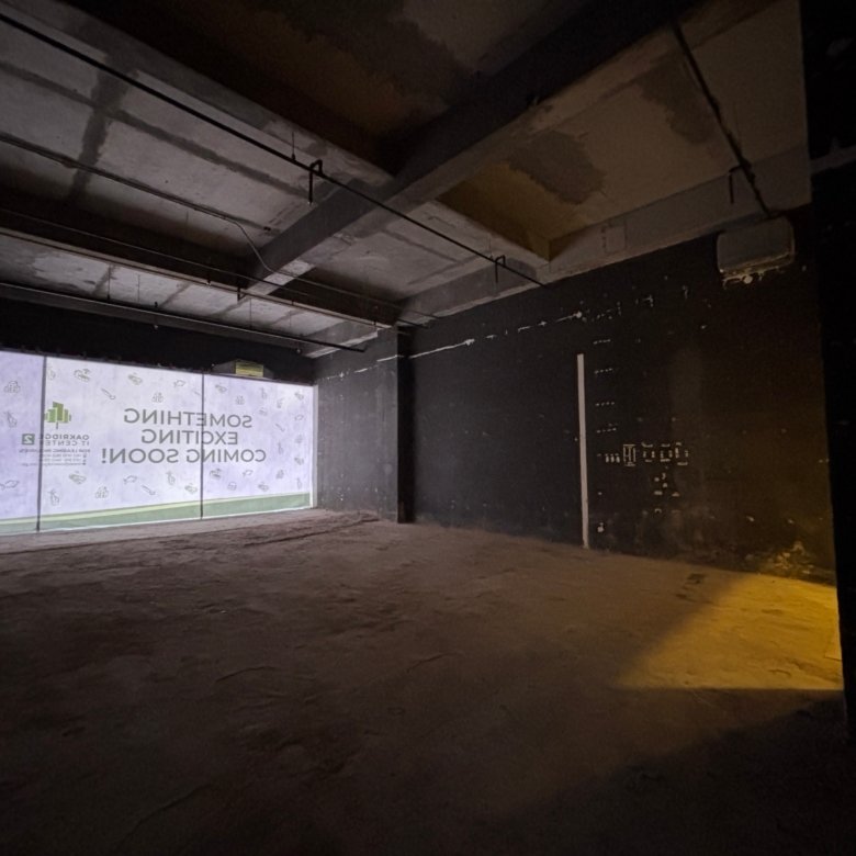 Dimly lit interior of a construction site with exposed concrete beams, pipes, and a dark wall; appears unfinished and industrial at night.