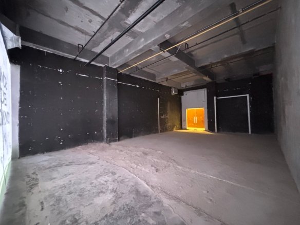 Dim concrete underground corridor with exposed pipes and a glowing orange exit at the far end.