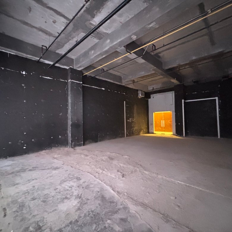 Dim concrete underground corridor with exposed pipes and a glowing orange exit at the far end.