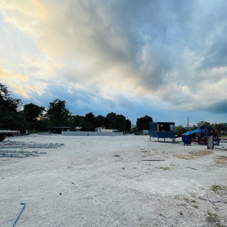 Open construction yard with scattered concrete blocks, trucks, and blue containers under a cloudy sky.