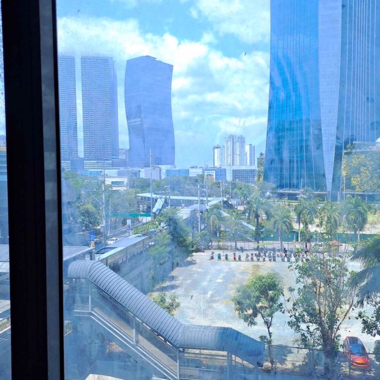 City skyline featuring blue glass skyscrapers and a curved elevated walkway among palm trees.