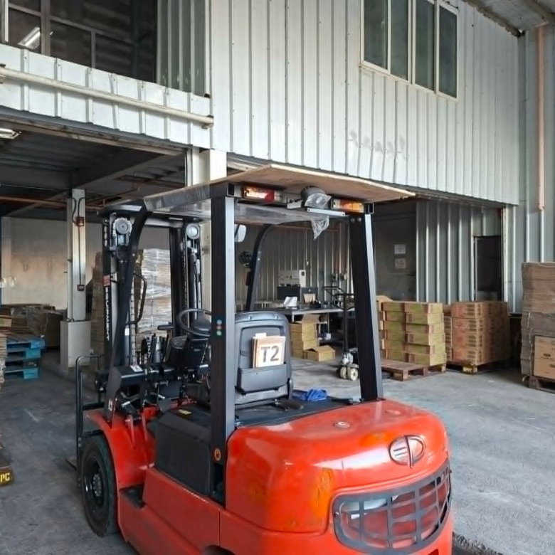 Orange forklift in a warehouse, with stacked pallets and metal shelving nearby.