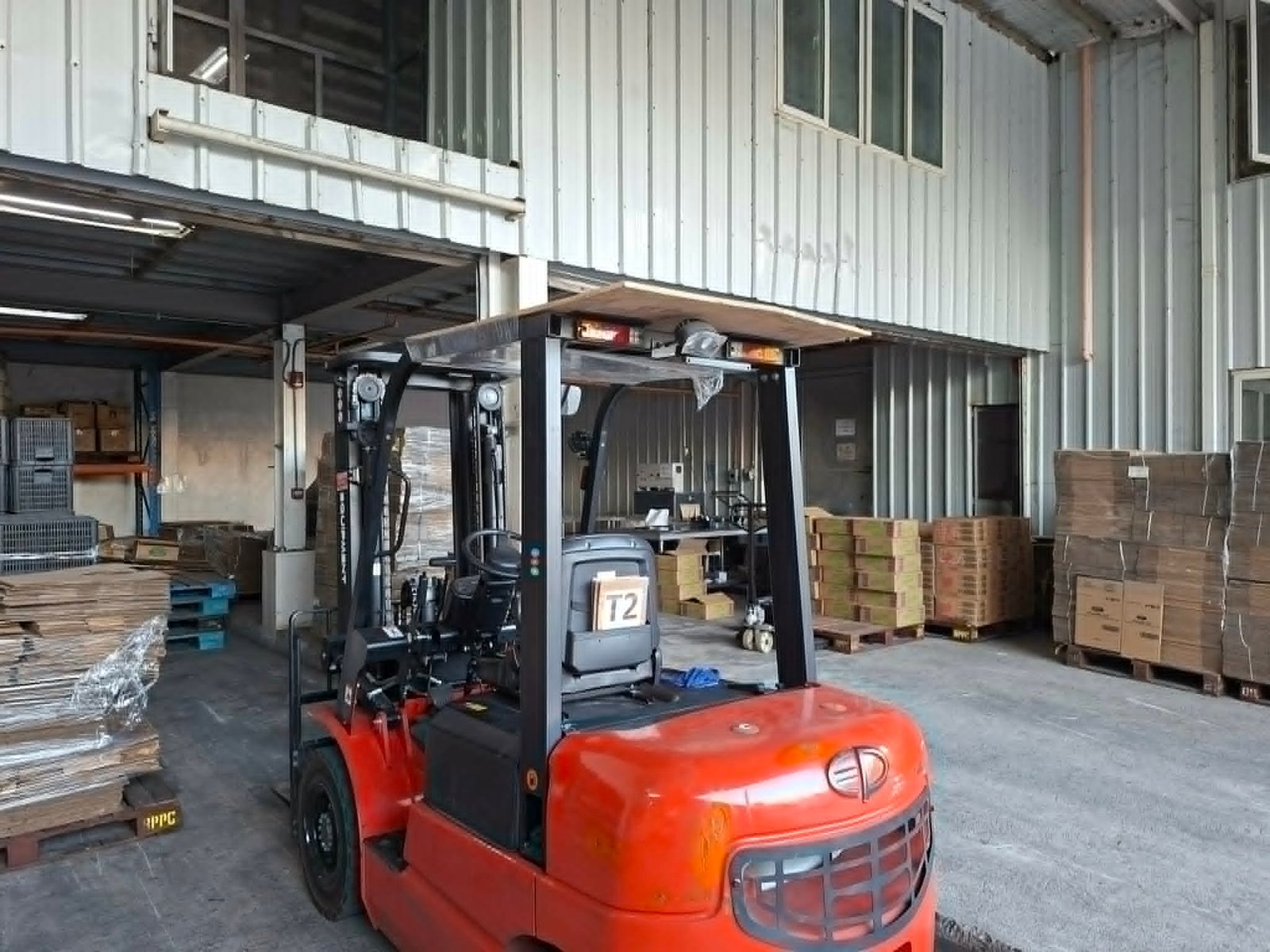 Orange forklift in a warehouse, with stacked pallets and metal shelving nearby.