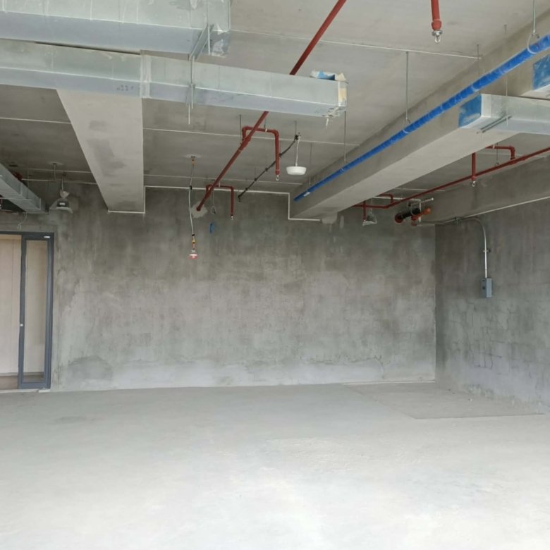 Unfinished industrial room with exposed pipes and ducts, concrete walls, and a glass door on the left side.