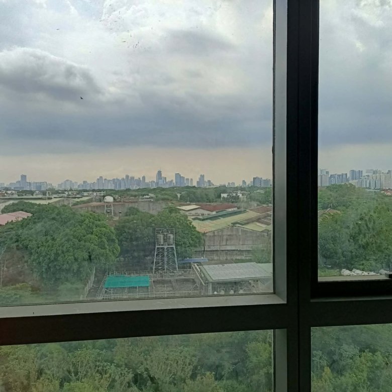 City skyline visible through a large window, with trees in the foreground and a cloudy sky above.