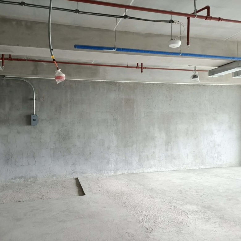 Unfinished concrete room with exposed pipes on the ceiling and a small electrical box on the left wall.