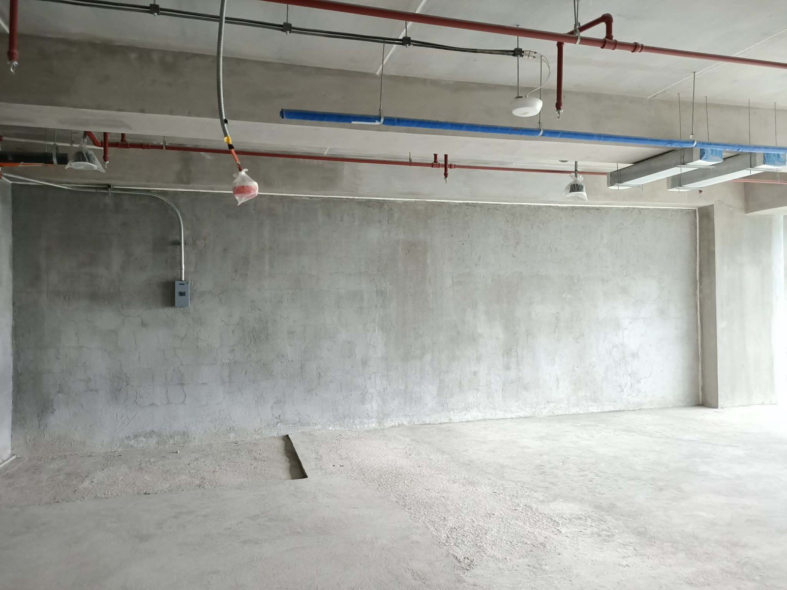 Unfinished concrete room with exposed pipes on the ceiling and a small electrical box on the left wall.