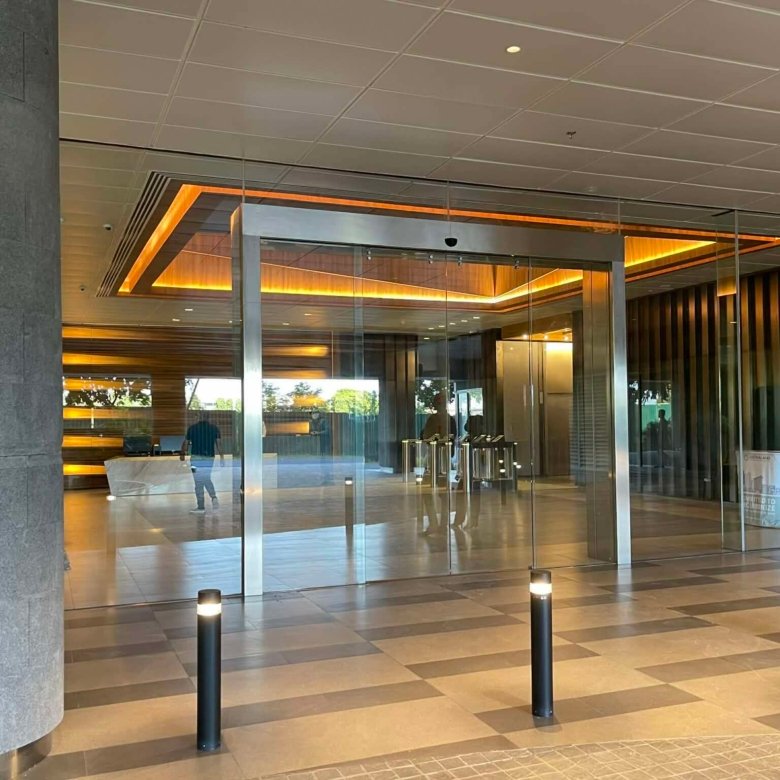 Modern office lobby with glass revolving doors, warm orange backlighting, and a man in a plaid shirt standing to the right near the entrance.