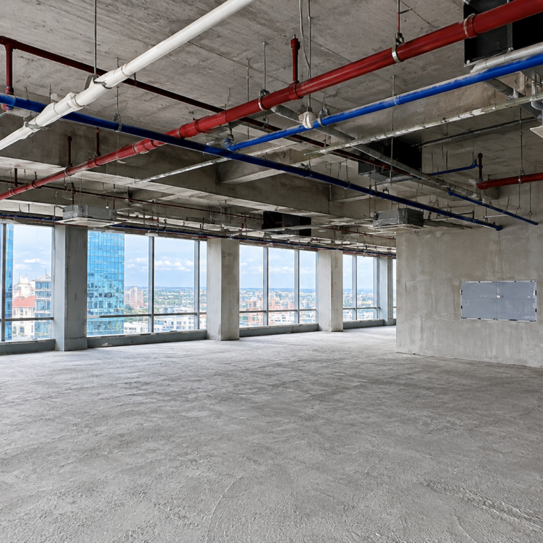 Empty unfinished office space with exposed red and blue pipes, concrete pillars, and large windows overlooking the city skyline.